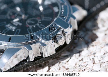 Mechanical watches with shiny metal casing and leather strap lie on the sand