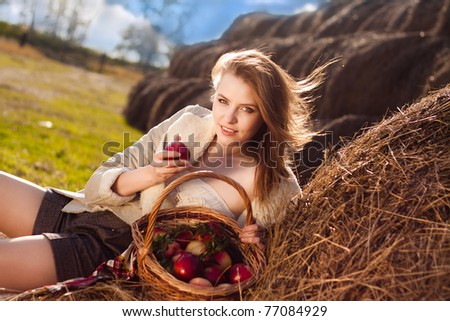 beautiful blonde smiling woman with many apple in basket on haystack at farm