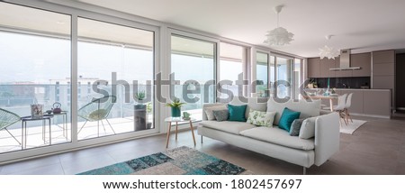 Modern living room with designer furniture. Sofa with light cushions and balcony view. Behind the modern kitchen with island. Nobody inside. 