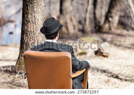 man alone in the woods sitting on a vintage armchair, rear view