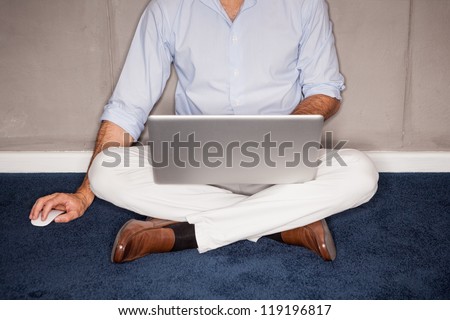 Man sitting on floor with laptop in office - landscape interior.