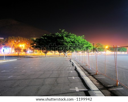Illuminated tree and fence at night in stadium parking lot.