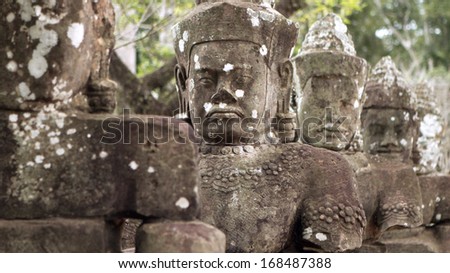 SIEM REAP, CAMBODIA - AUGUST 25: Stern faced warriors, carved in stone, guard the entrance to Angkor Wat on August 25, 2012 in Siem Reap, Cambodia.