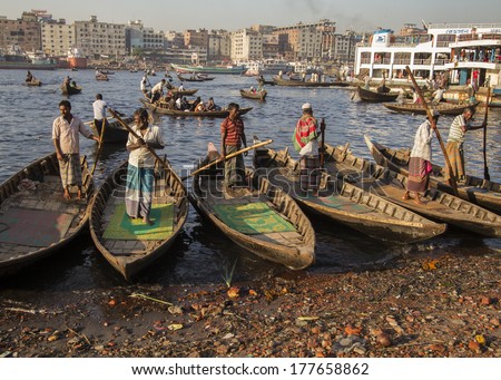 DHAKA, BANGLADESH - FEBRUARY 15, 2013: Men stand in their boats, waiting for clients to take across the Buriganga River.  Dozens of craft ply the waters of the river carrying passengers and cargo.