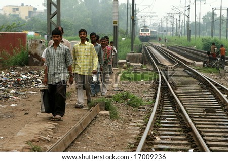 NEW DELHI, INDIA - JULY 2008: Indian men walk to work along a train line in the early morning.