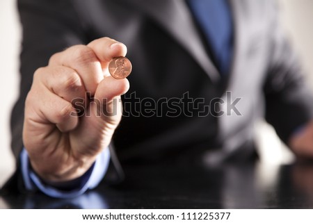 A businessman dressed in a suit holds a shiny penny in his hand.