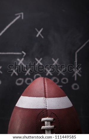 An American football with a play drawn up on a chalkboard in the background.