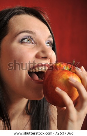 A portrait of a girl biting a red apple excitingly
