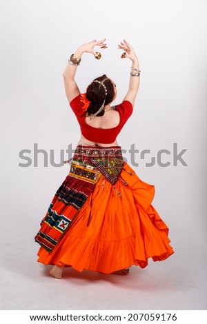 young brunette tribal dancer in national turkish costume dancing with her orange skirt flying on gray background in studio