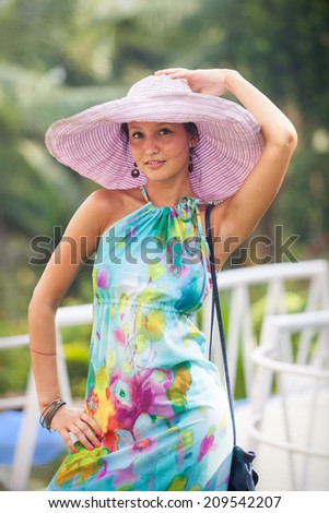 beautiful brunette young girl in style flower dress and big pink hat standing and posing  on white rock bridge and smile at the camera