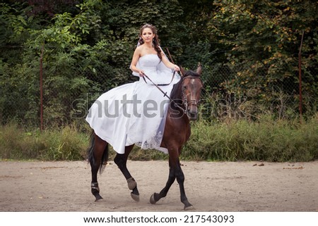 young charming brunette bride in white wedding dress and tracery veil rides on horse