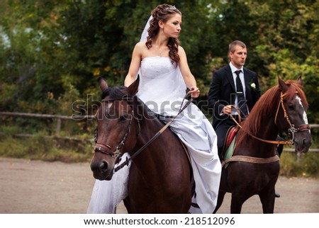 young charming brunette bride in white wedding dress and handsome groom in black suit rides on horses