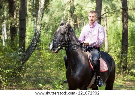 handsome man in pink shirt ride on the black horse in green forest