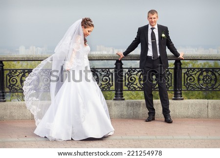 beautiful brunette bride in white wedding dress and young handsome groom in black suit stand on big city background