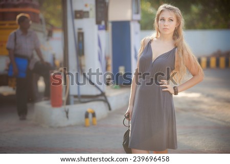 beautiful blonde girl in gray dress and handbag stand on petrol station
