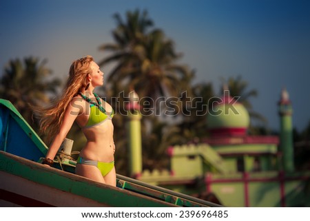 beautiful blonde girl in green swimming suit pose at the boat with green mosque on background