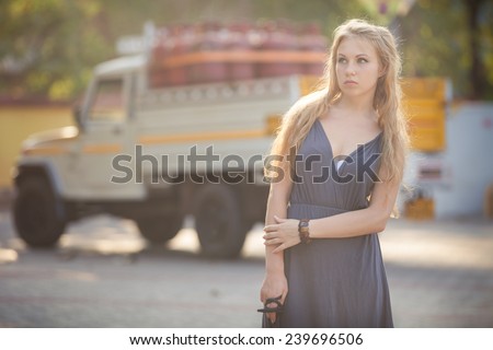 beautiful blonde girl in gray dress and handbag stand on petrol station
