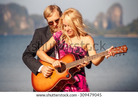 blonde girl in red with  guitar by bearded guitarist on beach at low tide