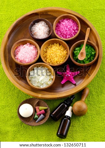 color sea salt in wooden bowl with cherry flower ,massage oil ,spoon on green towel