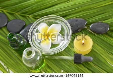 White plumeriaon bowl and stones ,massage oil ,candle and palm leaf
