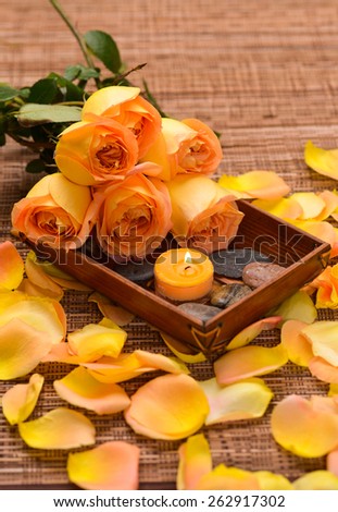 Set of orange rose and petals with white candle in basket on mat