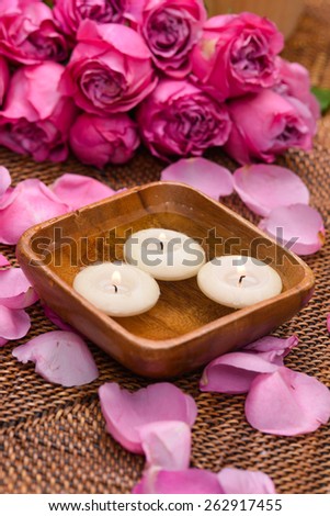 Lying down rose and petals with white candle in bowl on mat