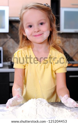 Cute blond little girl making bread in the kitchen