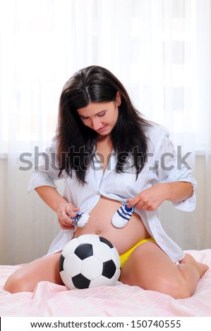young pregnant woman with a soccer ball and athletic shoes for baby. waiting for the boy