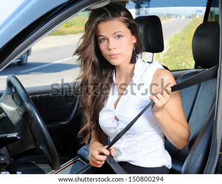 An attractive young Caucasian woman fastening her seat belt before the car trip on the front seat of the car