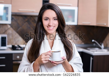 Kitchen Woman. Portrait of young smiling woman holds a cup with coffee or tea against kitchen background.
