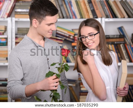 Love in the library. Young student boy gives a flower to a young student girl