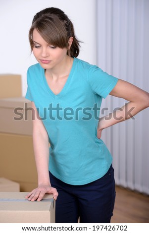 Pain in back. Young woman holding hand on his back and expressing negativity while leaning at the cardboard box