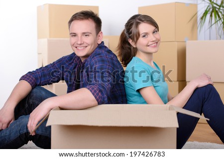 Moving to a new apartment. Beautiful young couple standing close to each other and smiling at camera while holding cardboard boxes