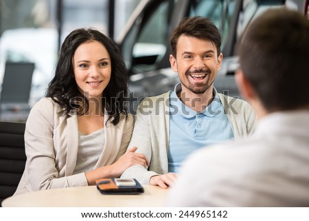 Some paperwork before buying a car. Young car salesman talking to a couple in auto salon.