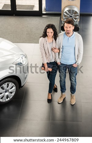 Beautiful young couple in the showroom, choosing a car. Top view.