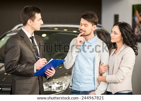 Handsome young car salesman is standing at the dealership telling about the features of the car to the customers.