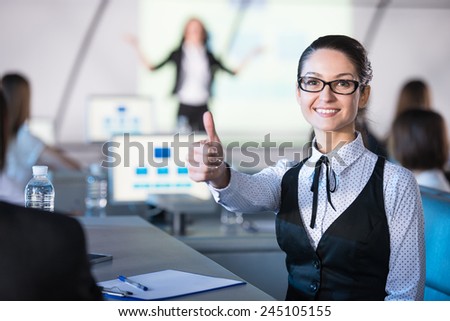 Young smiling business woman is looking at the camera during presentation in modern conference hall.