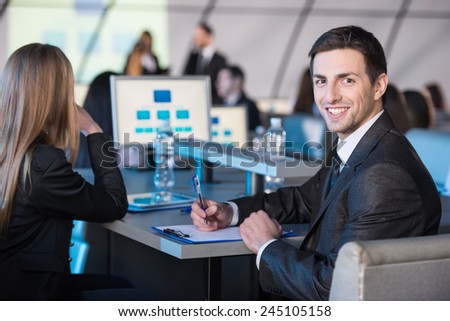 Young handsome business man is looking at the camera during presentation in modern conference hall.