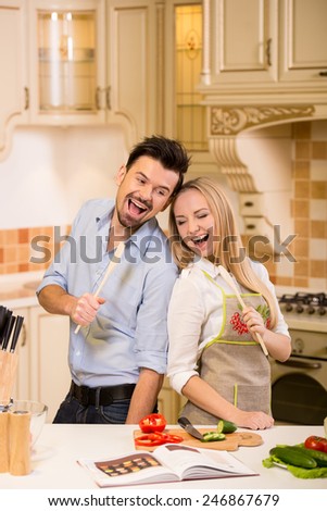 Beautiful, young couple in the kitchen are singing while cooking.
