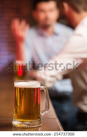 Two male friends in a pub with glasses of beer. Focus on a glass of beer.