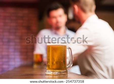 Two male friends in a pub with glasses of beer. Focus on a glass of beer.