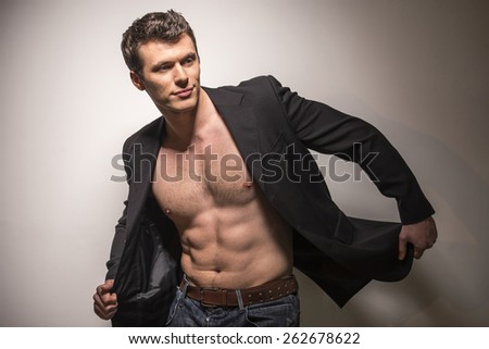 Young handsome man with open jacket is revealing muscular chest and torso. Isolated on light background.