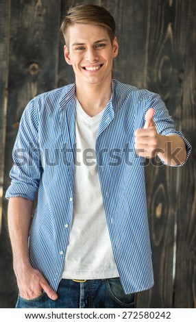 Waist up. Smilling young handsome man looking at camera and showing thumb up.