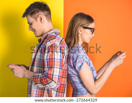 Portrait of young couple standing back to each other and looking at the phone.