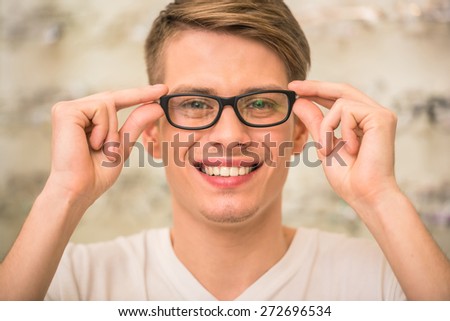 Young happy man in optician store is choosing glasses and looking at the camera.