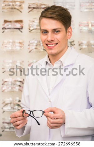 Optometrist is looking at the camera in glasses store. Professional young worker man.