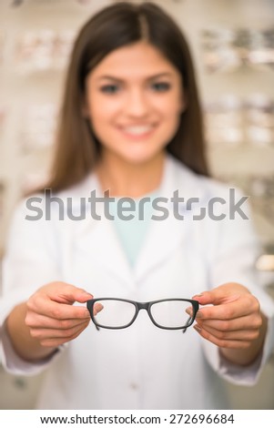 Optometrist is looking at the camera in glasses store. Professional young worker woman.