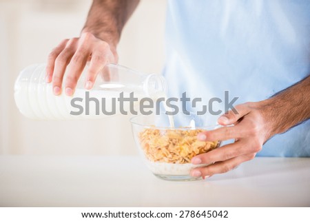 Close-up of man in blue t-shirt making corn flakes with milk for breakfast.