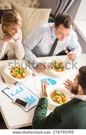 Three successful people sitting at the table and talking about business strategy during business lunch.