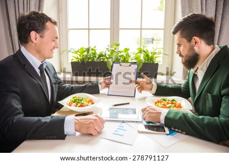 Two confident businessmen discussing contract at business lunch in cafe.